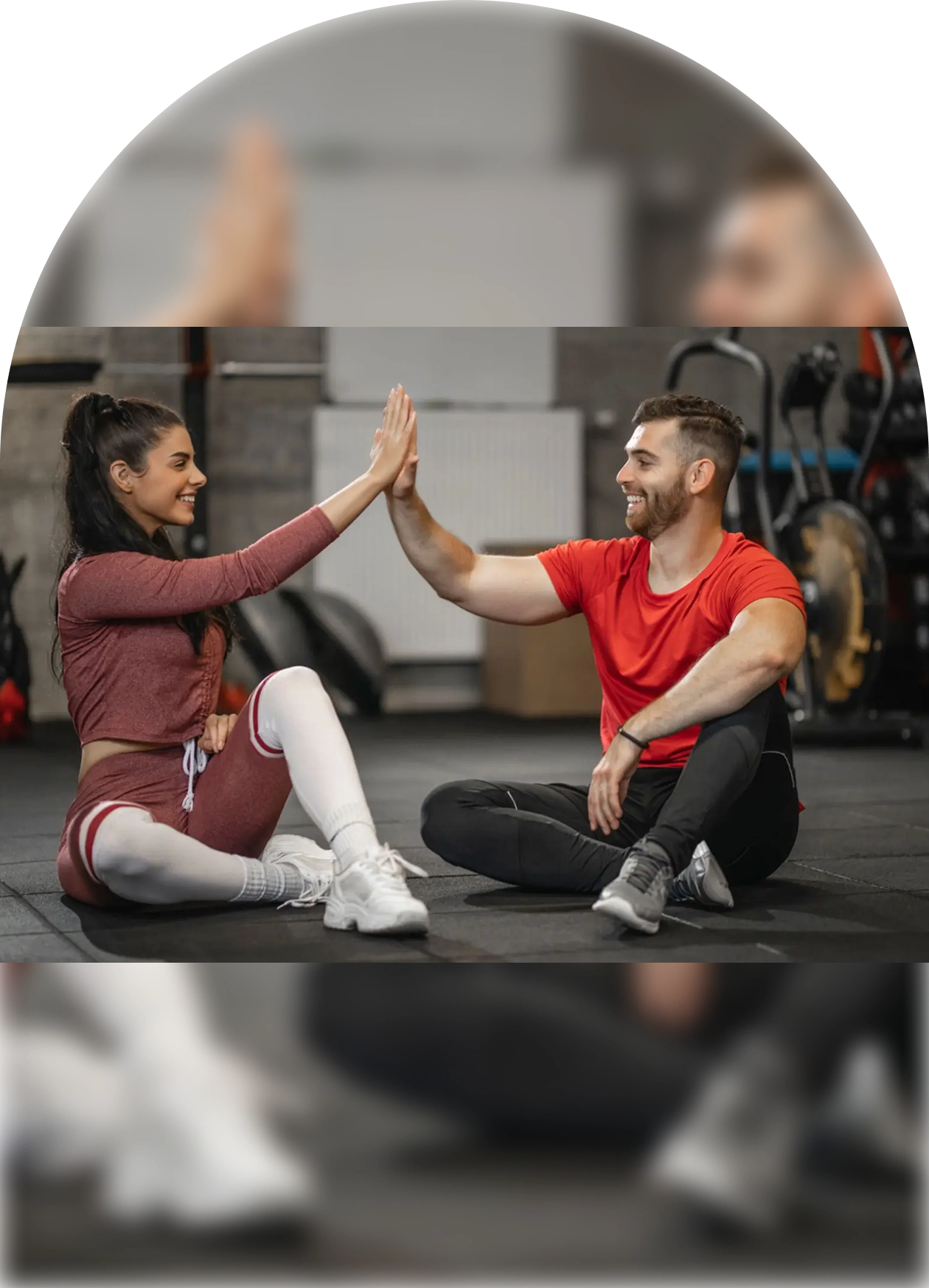 Two people sitting on yoga mats, high-fiving each other in a gym.