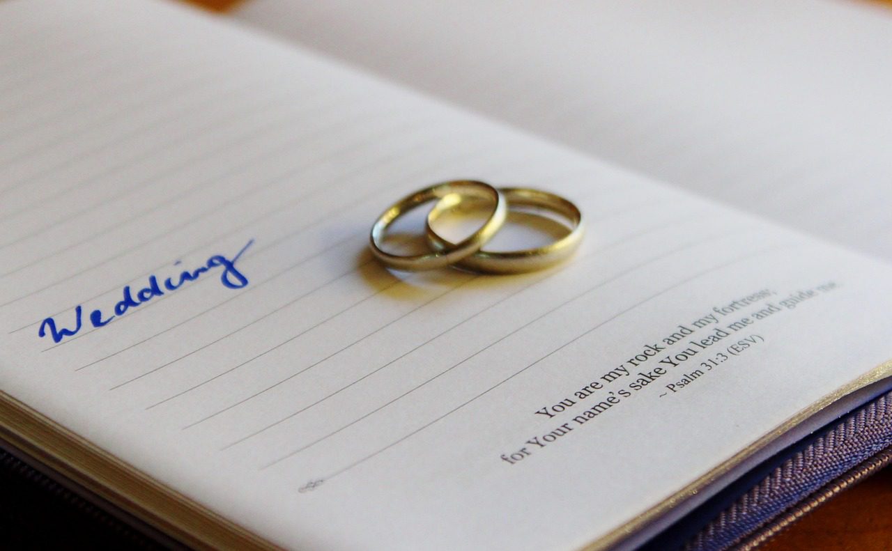 Two gold wedding rings resting on an open notebook with a heartfelt quote.